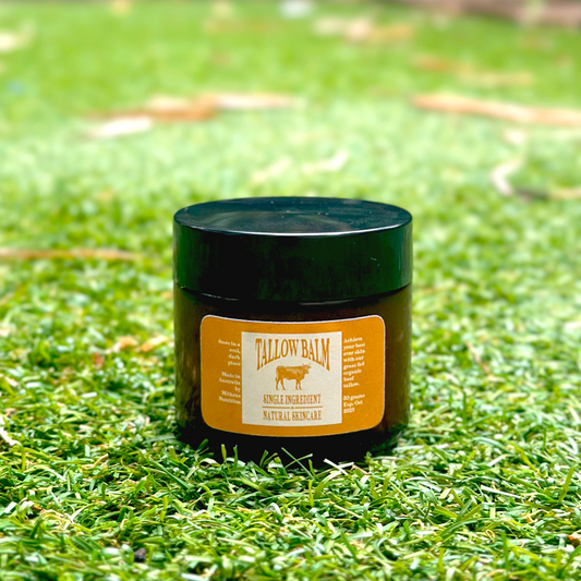 A jar of organic grass fed grass finished Australian Tallow Balm placed on grass. The label on the jar reads 'TALLOW Balm' and indicates it is a natural product